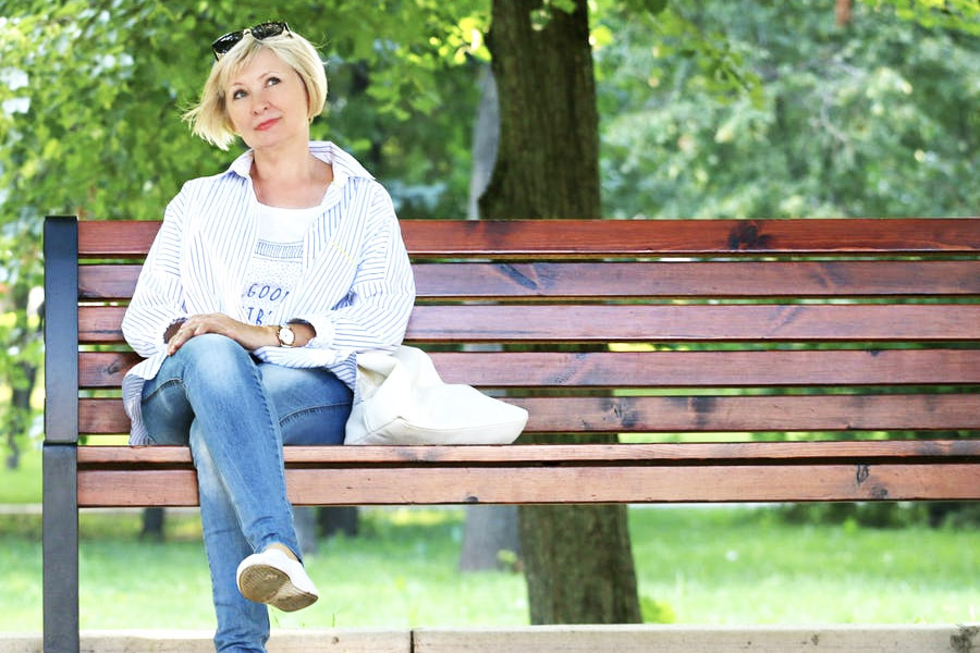 Older woman sitting on a bench in a park and smiling.